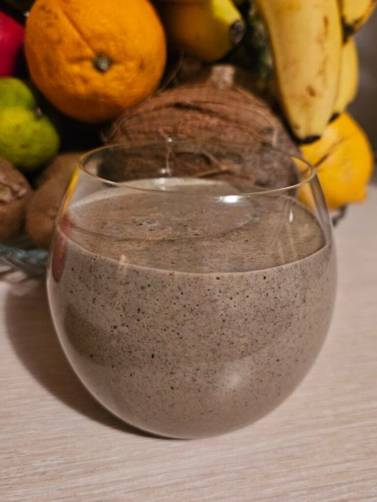 Glass of Moringa Walnuts Aronia Smoothie with fresh fruits in the background.