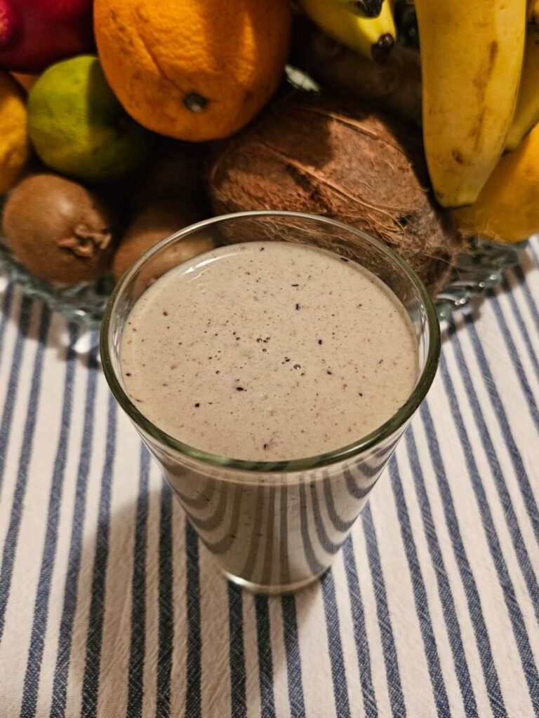 Glass of Berries Hazelnuts Spinach Smoothie with fresh fruits in the background.