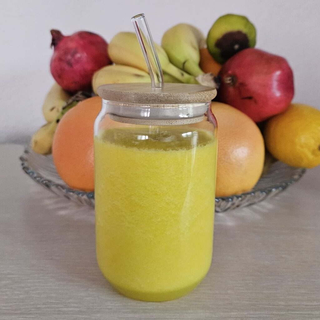 Golden Pineapple Cucumber Turmeric Juice served in a clear glass with fruits in the background.