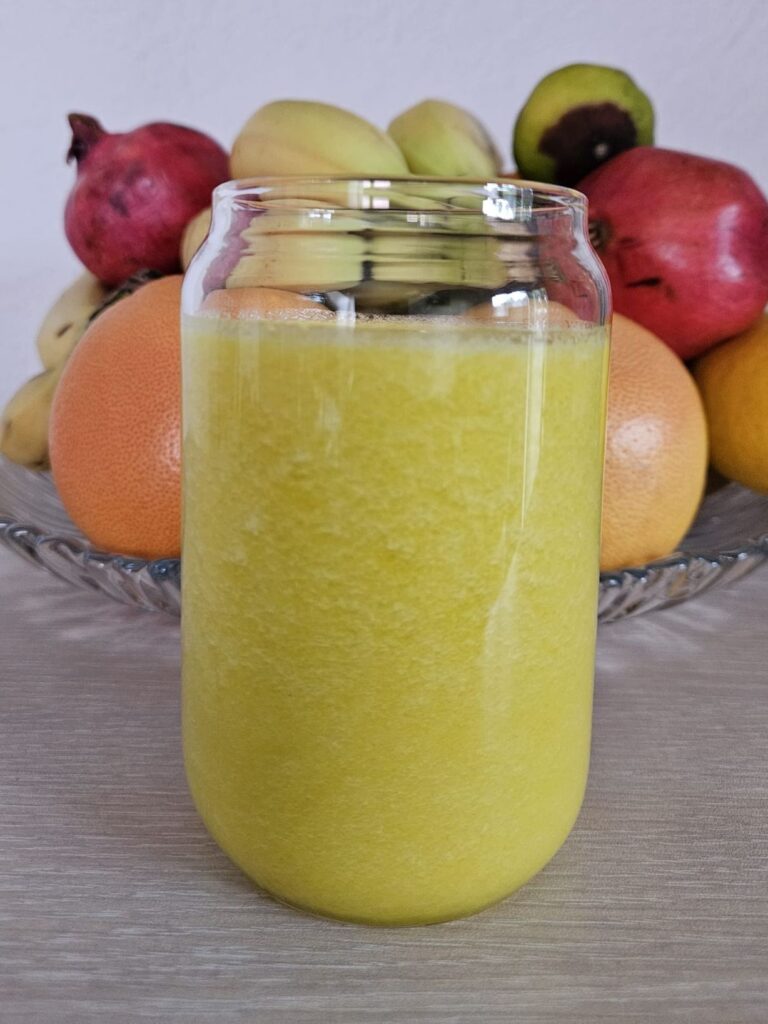 Glass of Pineapple Cucumber Turmeric Juice with fresh fruits in the background.