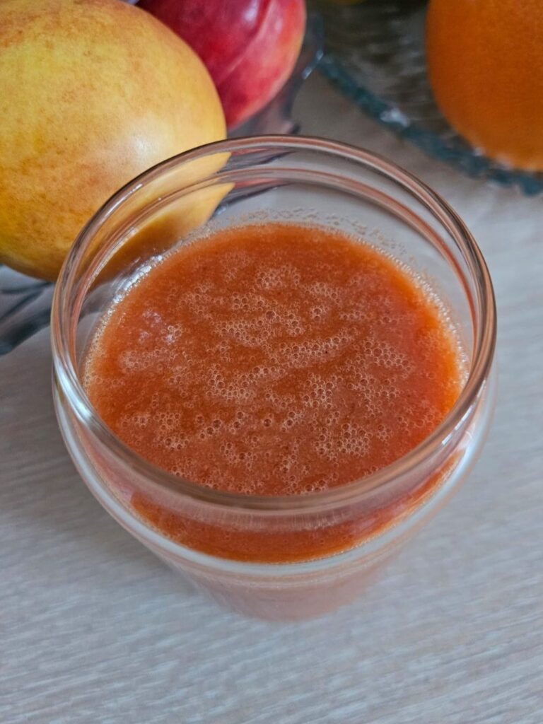 Glass of Carrot Strawberry Coconut Juice with fruits softly visible in the background.