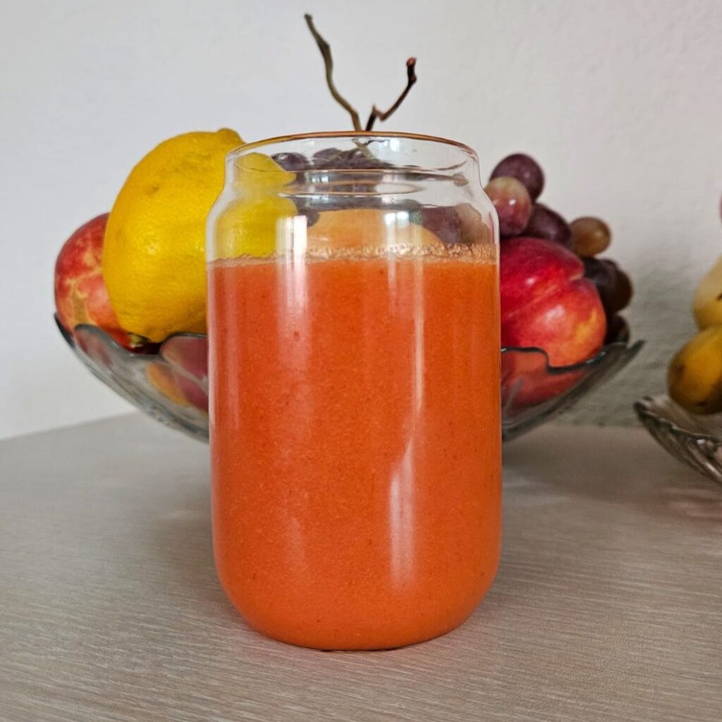 Orange Carrot Strawberry Coconut Juice served in a glass with fruits in the background.