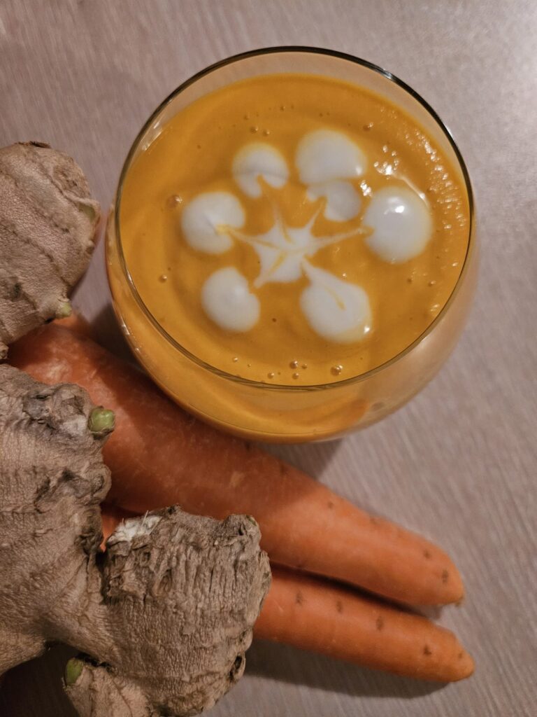 Overhead view of a glass filled with Apricot Carrot Ginger Smoothie surrounded by fresh carrots and ginger.