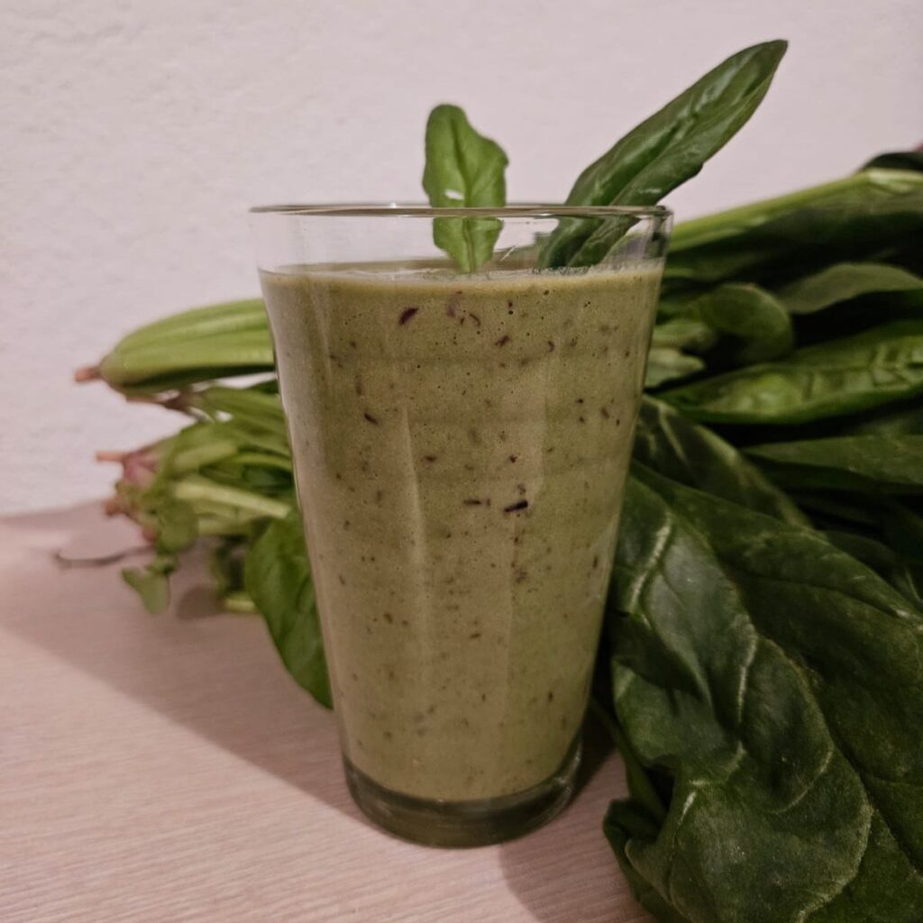 Glass of Black Currants Spinach Smoothie decorated with spinach leaves, with fresh spinach beside the glass.