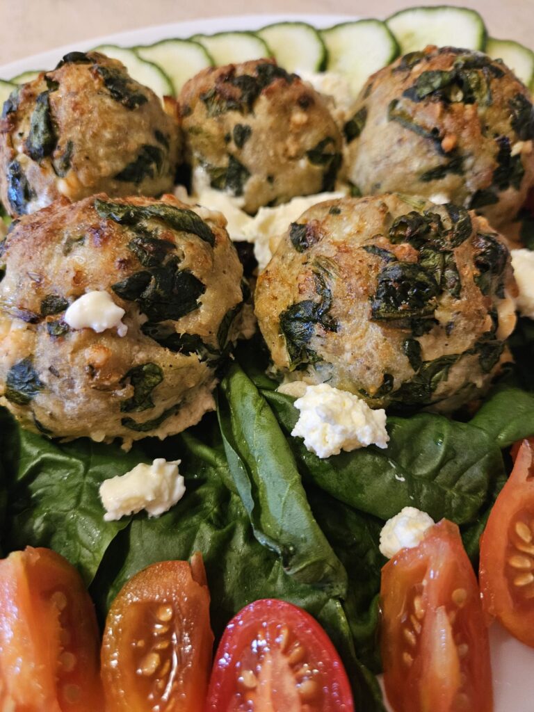 Close-up of a plate with baked turkey meatballs with spinach and feta, served with fresh tomatoes, spinach, and cucumber slices.