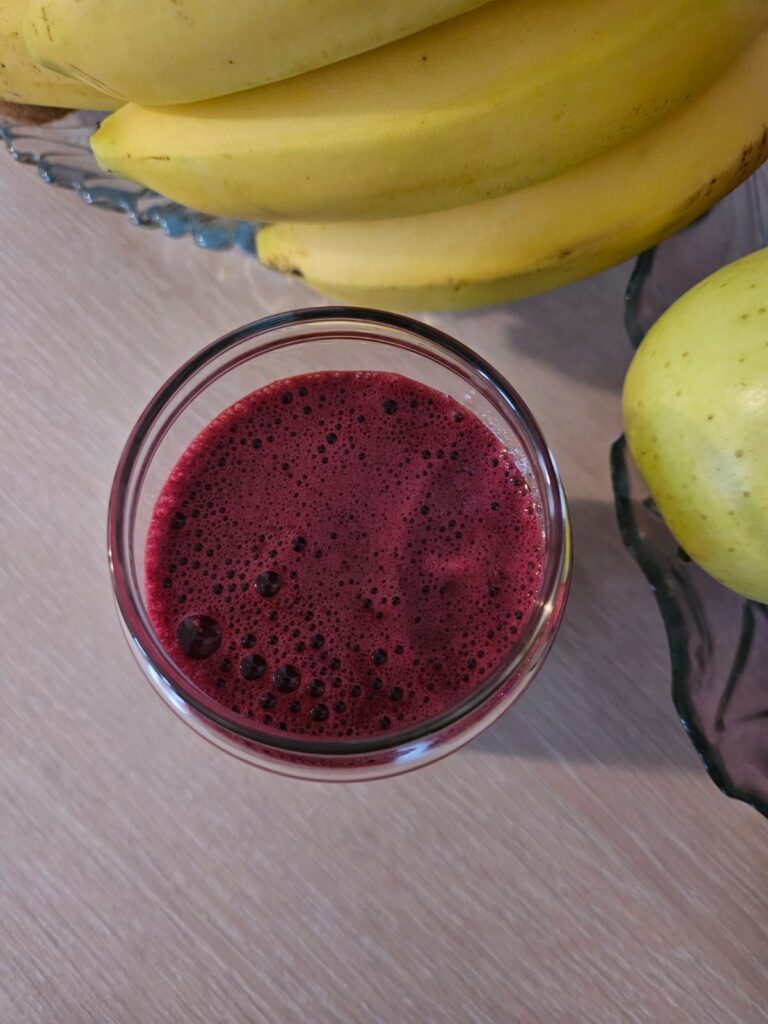 Top view of a glass with blueberry, beetroot and carrot juice, showing deep red color.