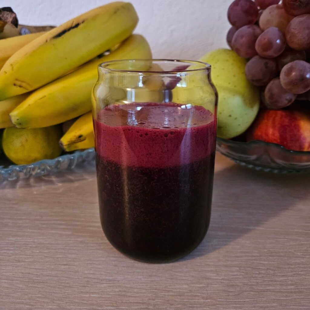 Side view of a glass filled with blueberry, beetroot and carrot juice showing its natural color.
