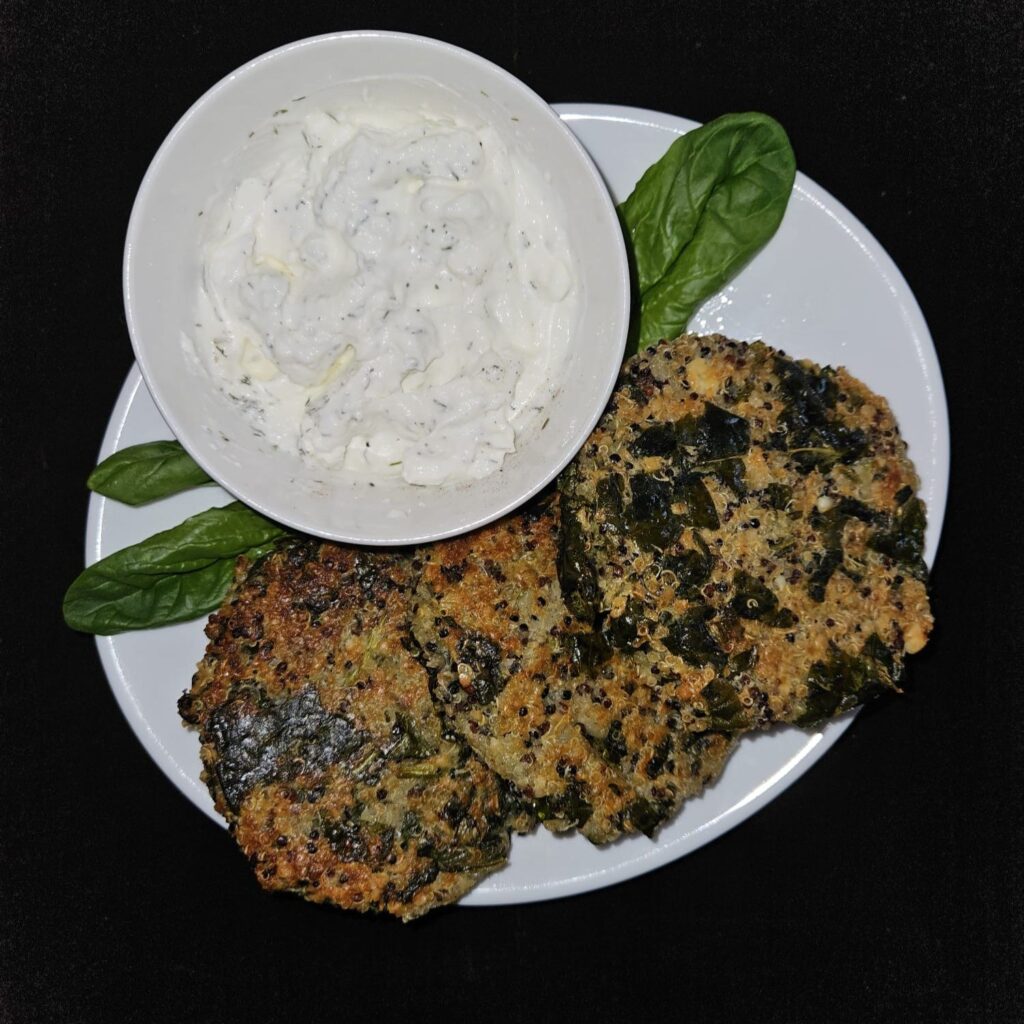 Served baked quinoa and spinach patties with yogurt dip, garnished with fresh spinach leaves on a plate.