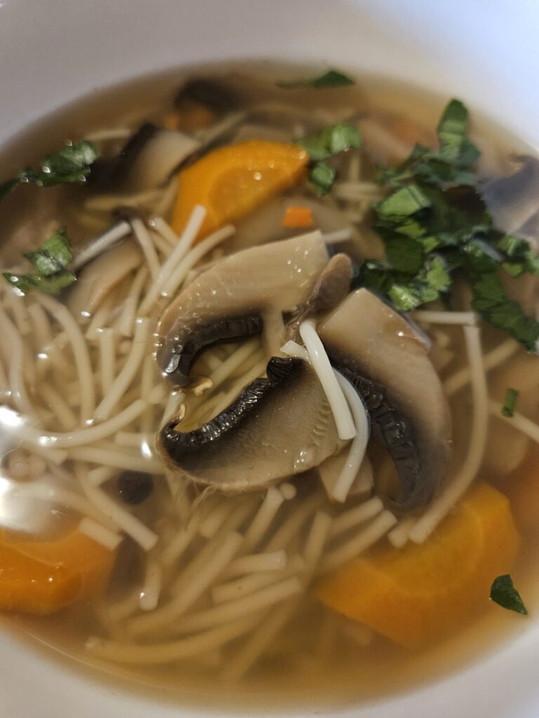 Close-up of clear mushroom and vegetable soup served in a white bowl.