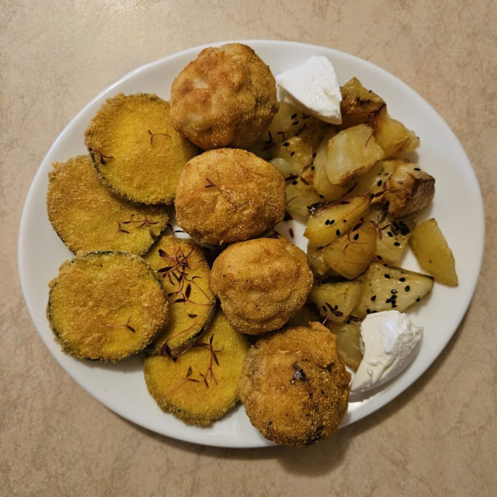 Served golden trio plate delight with chicken balls, zucchini slices, and potato cubes decorated with amaranth microgreens.