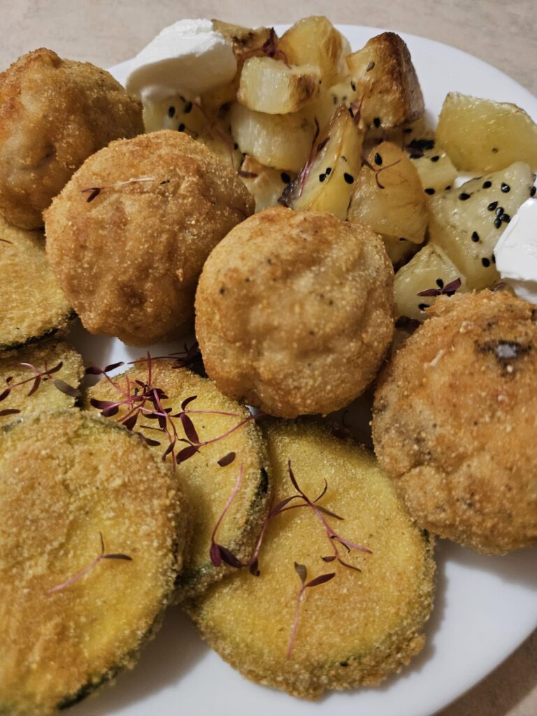 Close-up of a golden trio plate delight with chicken balls, zucchini slices, and golden potato cubes.