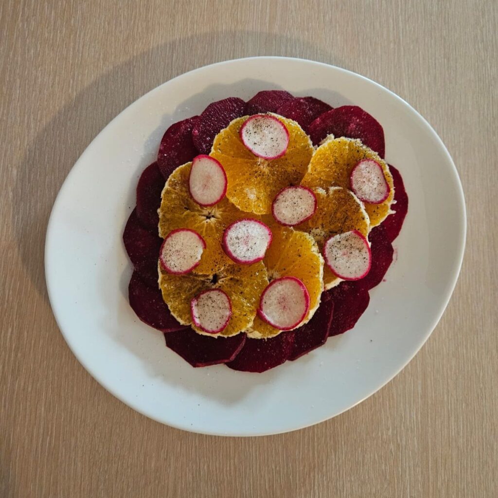 Plate with arranged slices of beetroot, orange, and radish.