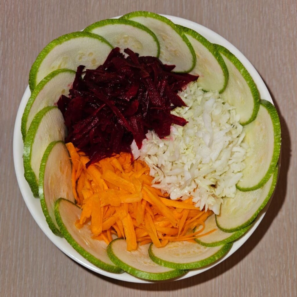 Overhead view of grated beetroot, carrot, cabbage, and thin zucchini slices arranged before adding dressing.