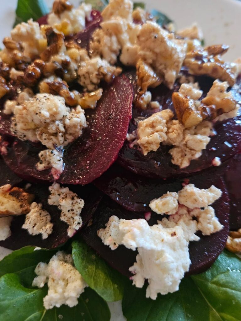 Close-up of beetroot salad with goat cheese, walnuts, and arugula on a plate.