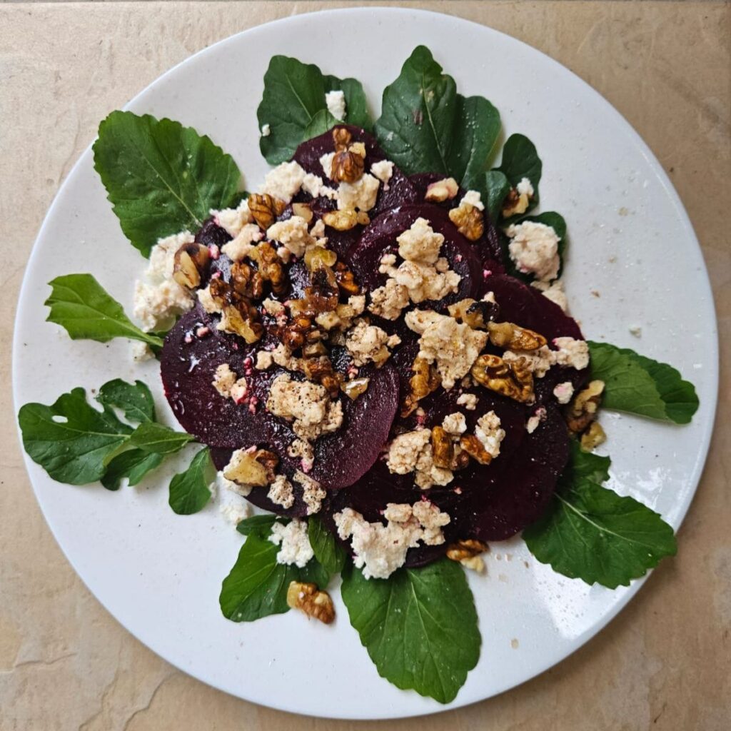 Overhead view of beetroot salad with goat cheese, walnuts, and arugula served on a plate.