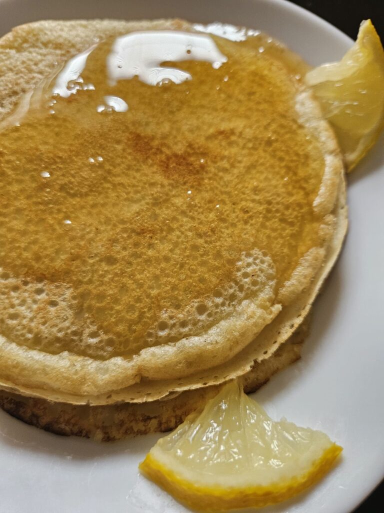 A stack of mini crepes drizzled with honey, photographed from the side up close.