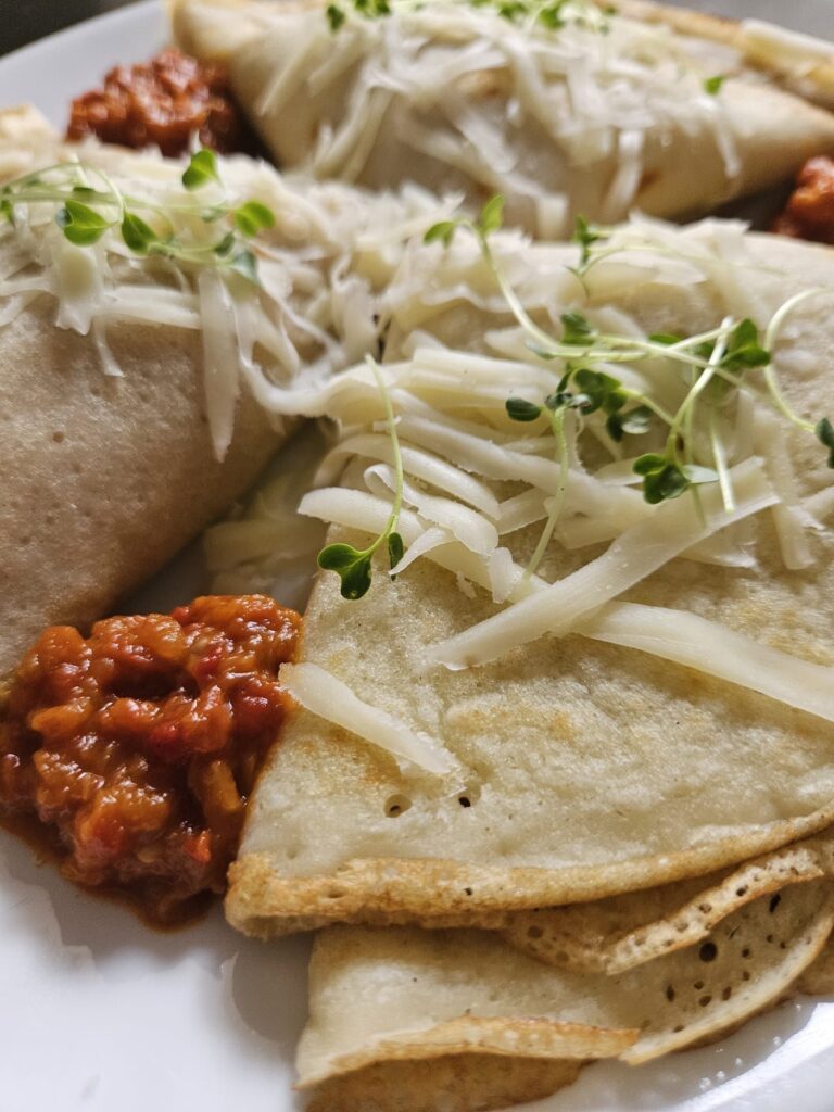 Close-up of folded savory crepes filled with ajvar, garlic, and cheese arranged on a plate.