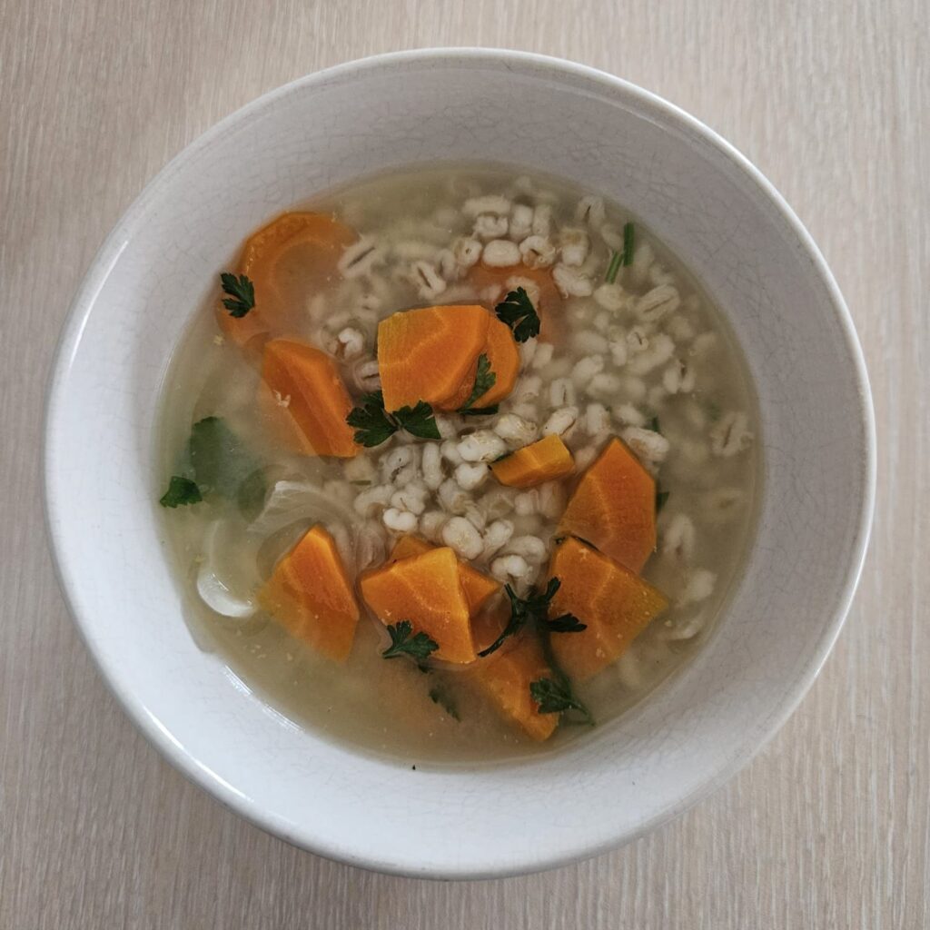 Barley Carrot Parsley Soup served in a bowl, viewed from above, showing vegetables and herbs.