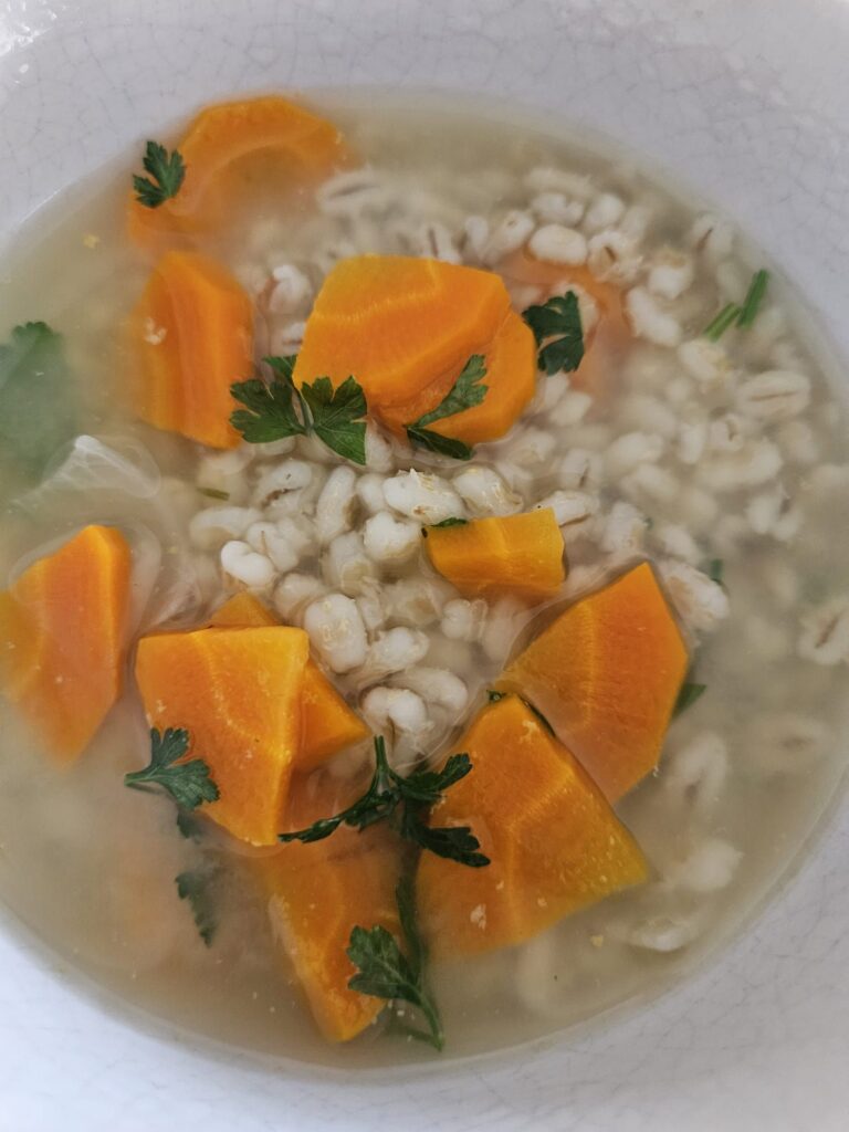 A close-up view of warm barley carrot parsley soup served in a bowl, showing its rich texture.