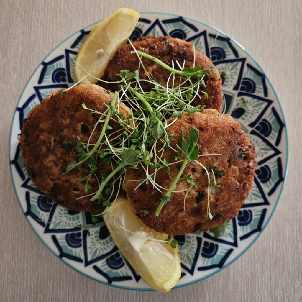 Salmon Cakes with Microgreens served with lemon slices on a plate.