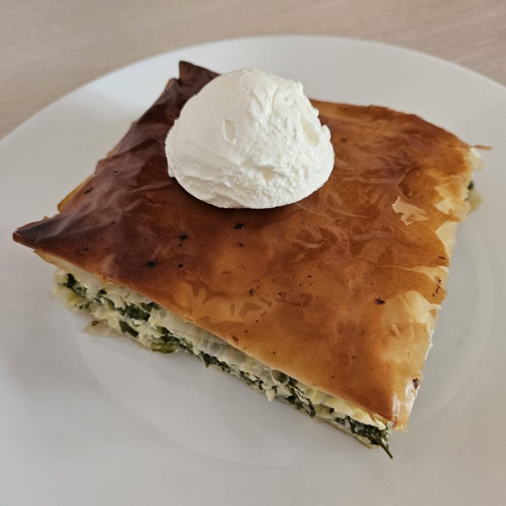 Slice of Spinach Cheese Pastry Delight served on a white plate with a scoop of cream cheese.