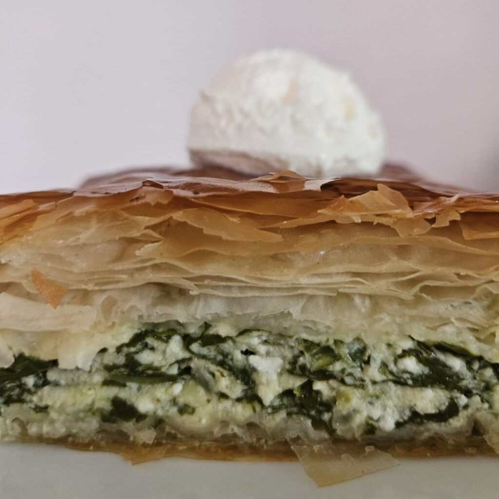 Side view of a slice of Spinach Cheese Pastry Delight served with cream cheese on a white plate. 