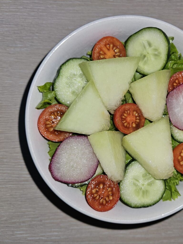 Close-up view of melon tomato green salad served in a bowl, showing its fresh colors and texture.
