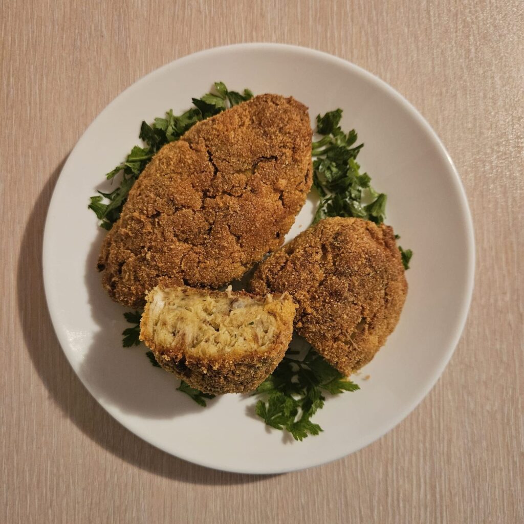 Two crispy mackerel cauliflower patties served on a plate and garnished with chopped parsley.