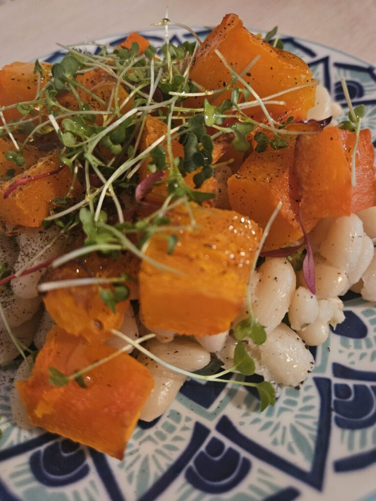 Close-up view of white beans, roasted pumpkin cubes, and vibrant microgreens arranged on a patterned plate.