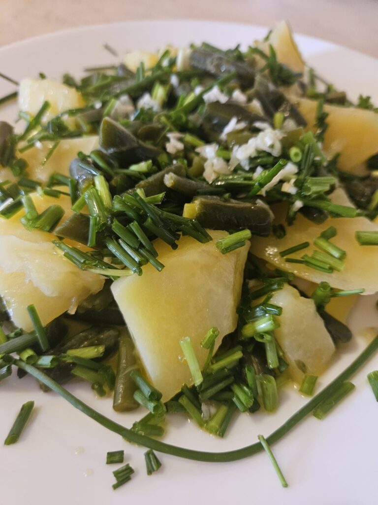 A close-up of boiled potatoes, green beans, and fresh chives neatly arranged on a flat plate.