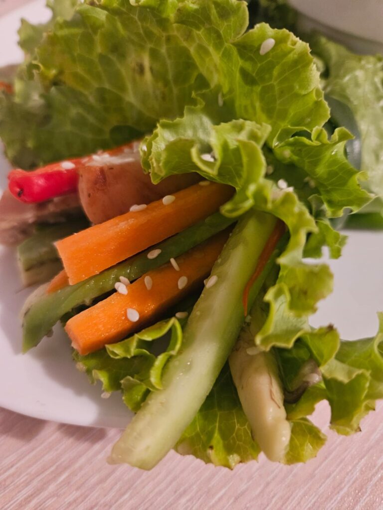 Chicken and vegetable wrap in lettuce leaves with avocado, carrot, and red pepper.