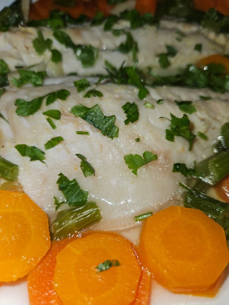 Close-up of a plate with Poached Fish with Carrots and Celery, showing tender fillets and colorful vegetables.