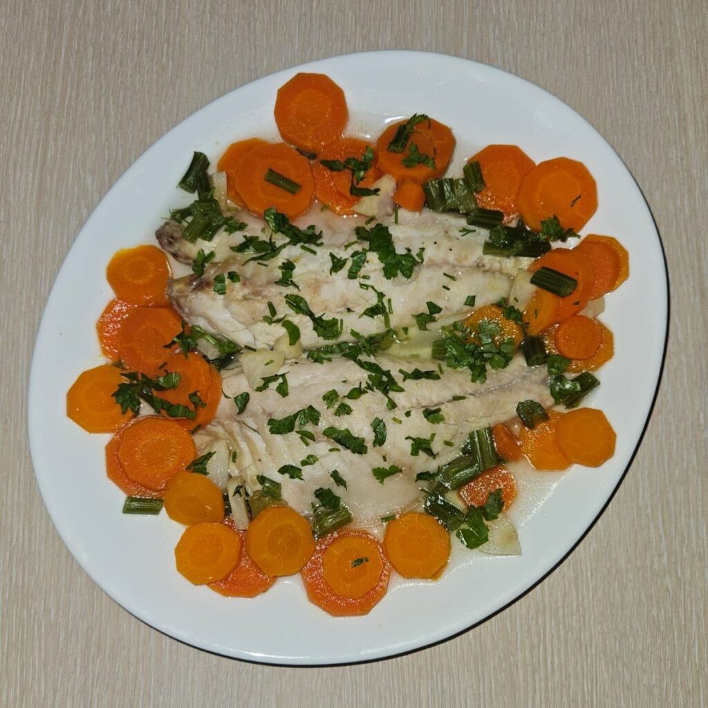 Poached Fish with Carrots and Celery served in a shallow white plate with clear broth and chopped parsley on top.