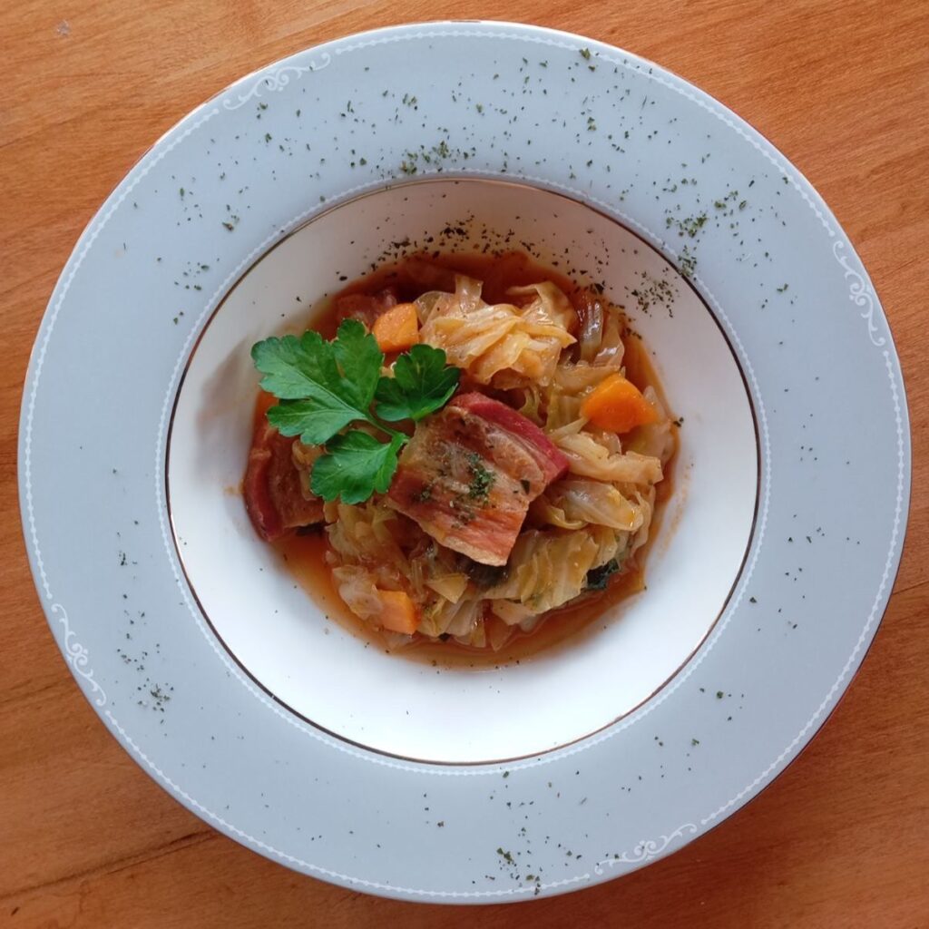 Wide plate filled with Savory Cabbage Pancetta Stew, garnished with parsley, ready to serve.