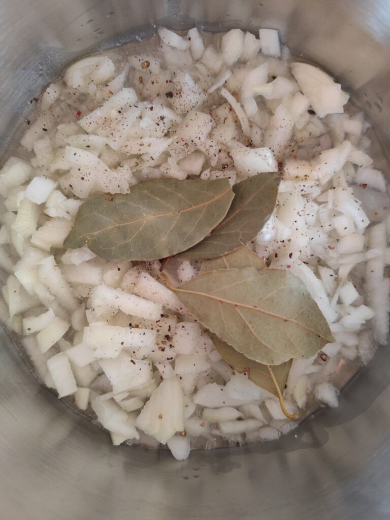 Chopped onions and bay leaves sautéing in a pot with oil, forming the flavorful soup base.