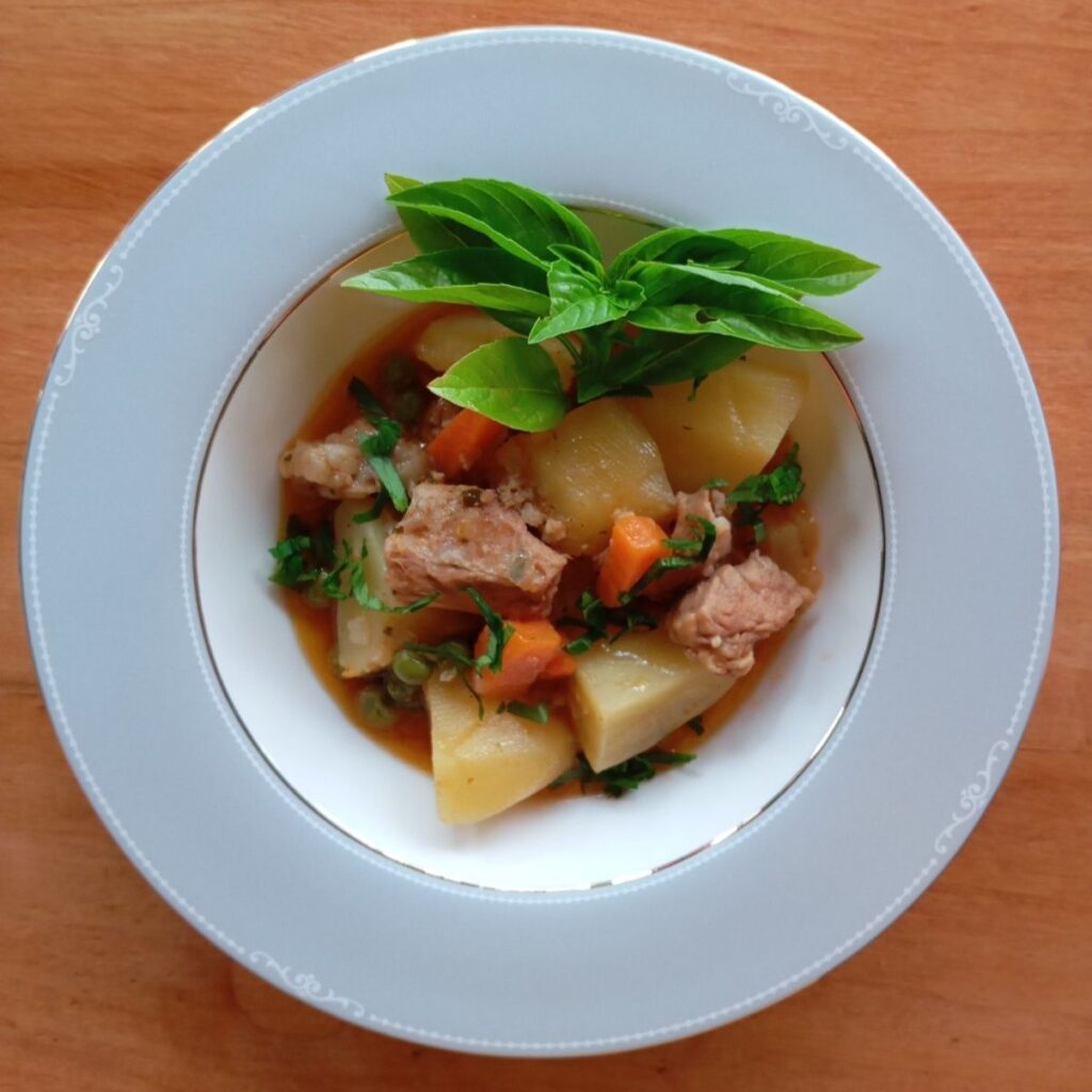 A wide, deep plate of Beef Pea Potato Stew garnished with chopped parsley and a sprig of basil.