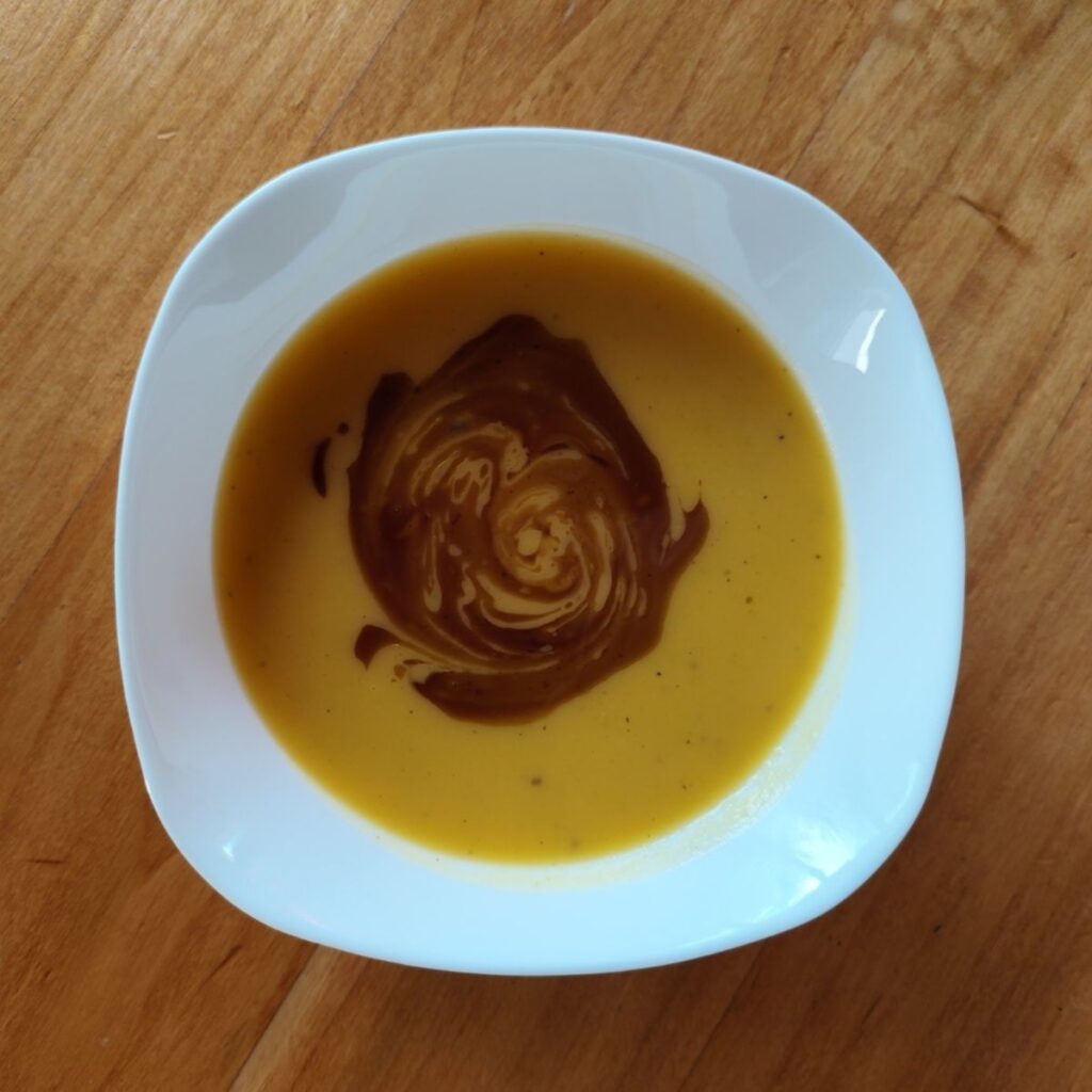Creamy Golden Butternut Squash Soup being blended smooth and served with pumpkin seed oil.