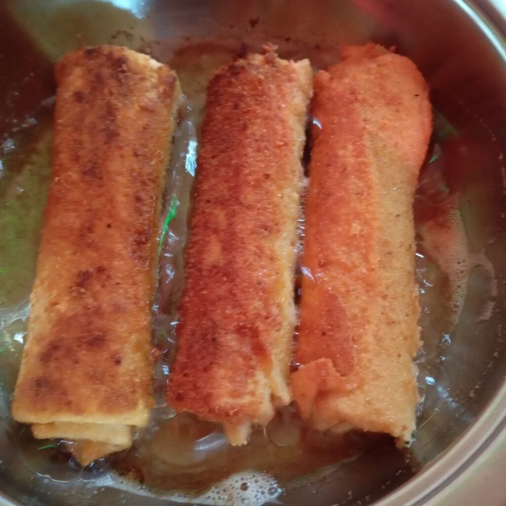 Three Crepe Rolls frying in a pan, turning golden and crisp during the cooking process.