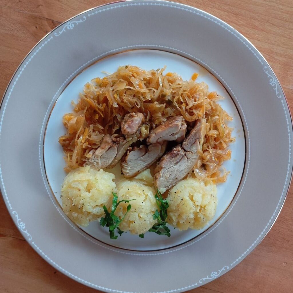 Single plate of Cabbage Chicken Potato Medley with braised cabbage, sliced fried chicken, and mashed potato balls, garnished with chopped parsley.