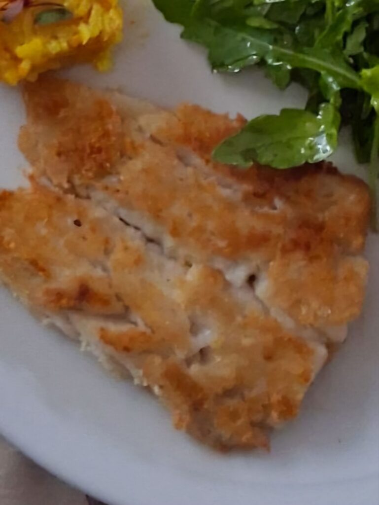 Close-up of baked hake fillet served on a plate, golden and lightly crisp.