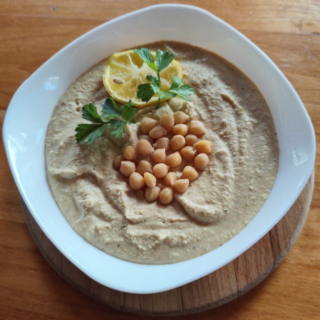 Chickpea spread served in a bowl decorated with whole chickpeas, parsley sprig, and a lemon slice.