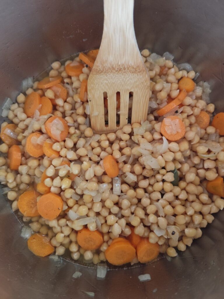Cooked chickpeas added to sautéed vegetables in a pot, mixing together for rich flavor.