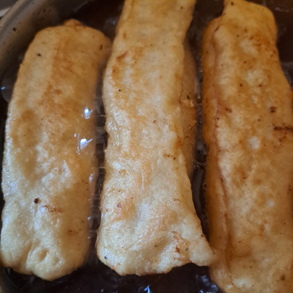 Piroshki frying in a pan with hot oil until golden and evenly cooked.