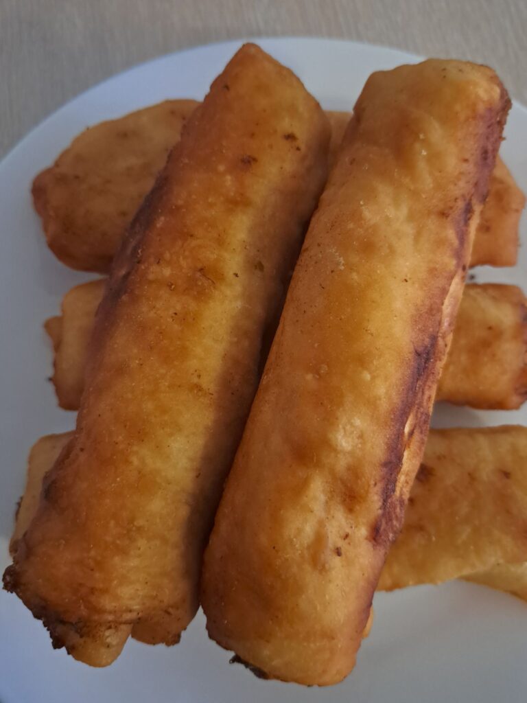 Five whole fried piroshki arranged on a white flat plate.