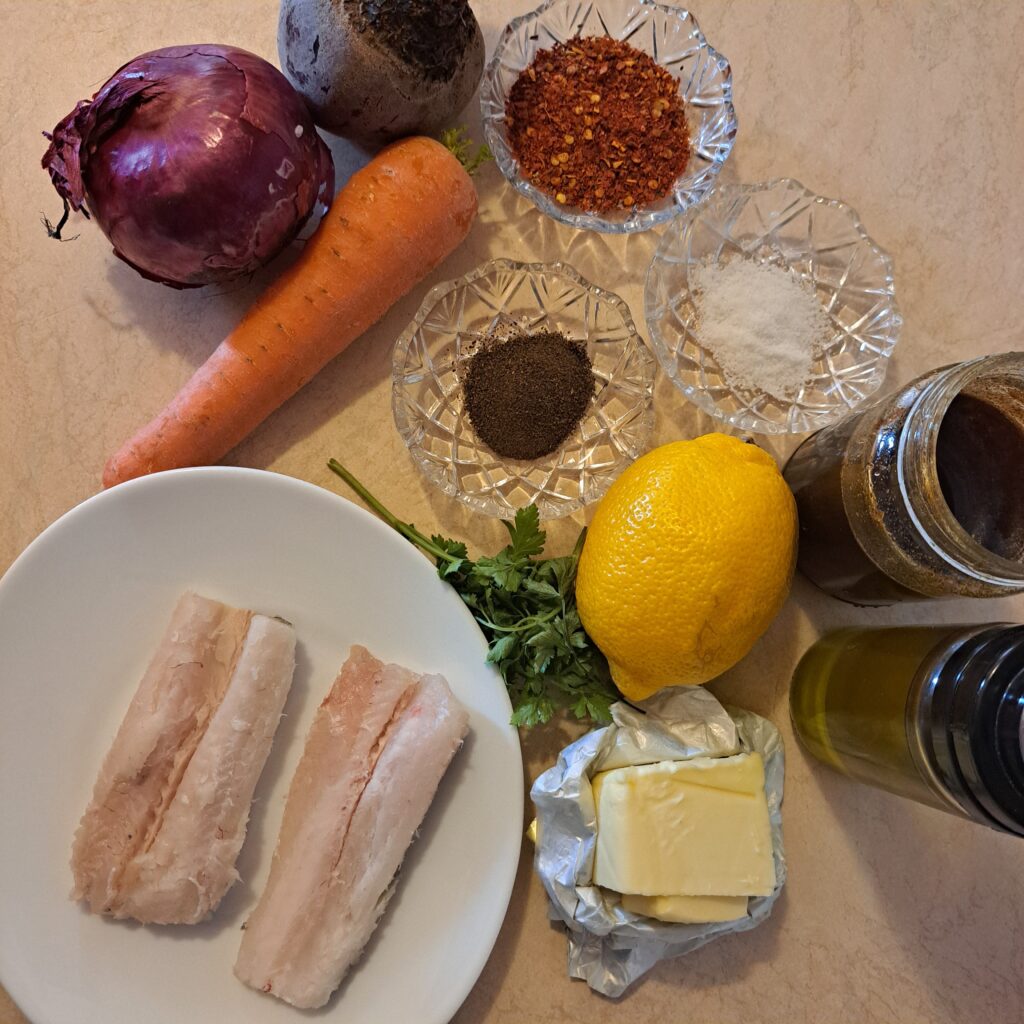 Two white fish fillets, beetroot, carrot, red onion, lemon, butter, honey, and spices arranged on a kitchen table.