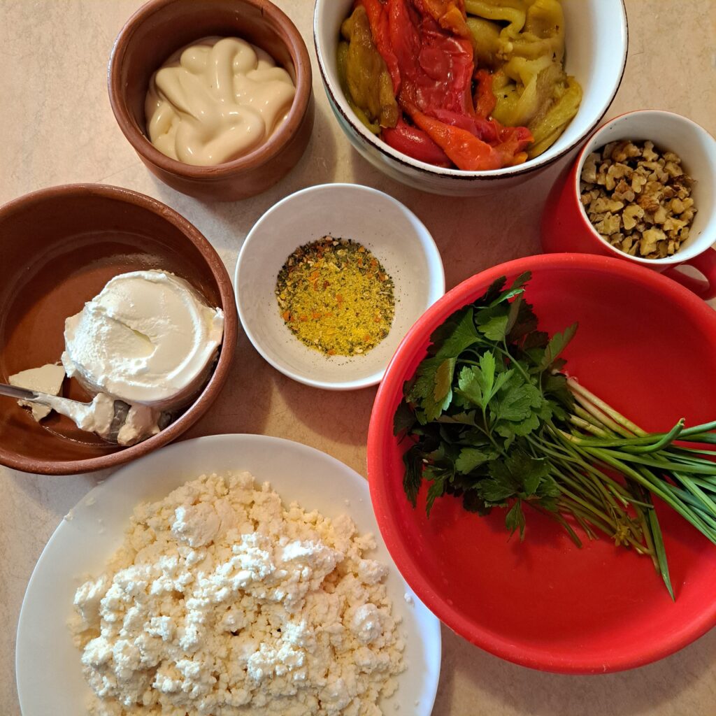 Ingredients for Roasted Peppers Walnut Salad on kitchen table: curd cheese, mayonnaise, sour cream, roasted peppers, walnuts, parsley, and seasoning.