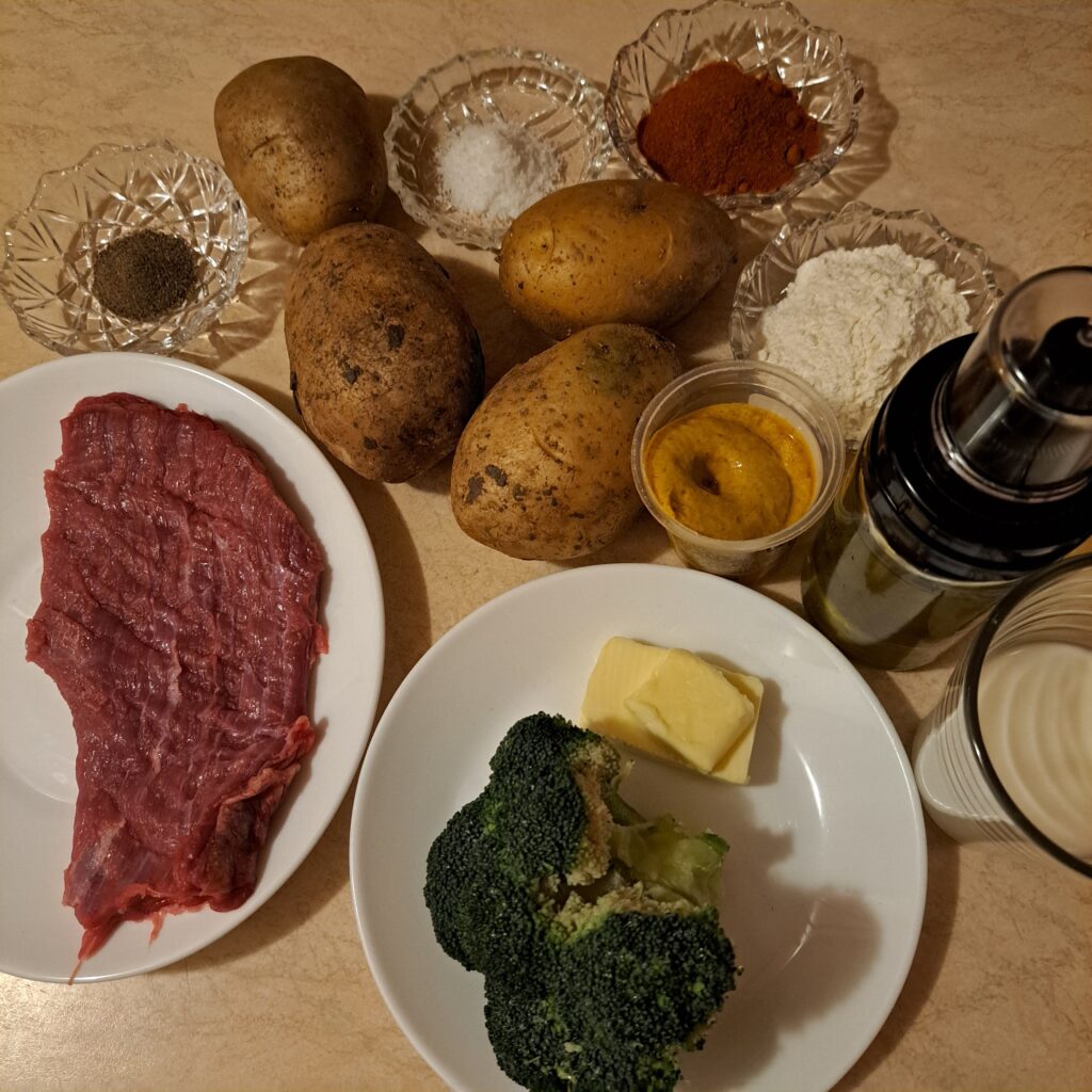 Ingredients arranged on a kitchen table: beef, broccoli, potatoes, butter, olive oil, milk, salt, black pepper, and ground red paprika ready for cooking.