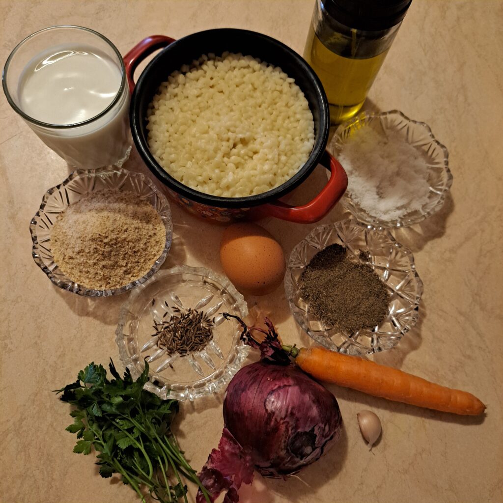 Cooked millet, carrot, red onion, garlic, yogurt, egg, cumin, parsley, salt, black pepper, olive oil, and breadcrumbs arranged on a kitchen table.