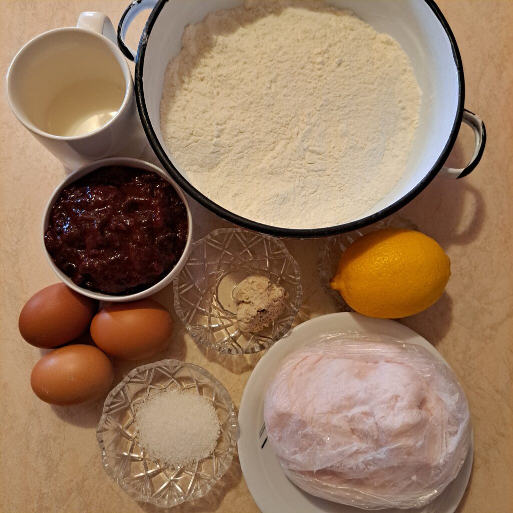 A neatly arranged set of ingredients for flaky lard homemade pastries, including flour, eggs, lard, milk, lemon, sugar, yeast, jam, and butter.