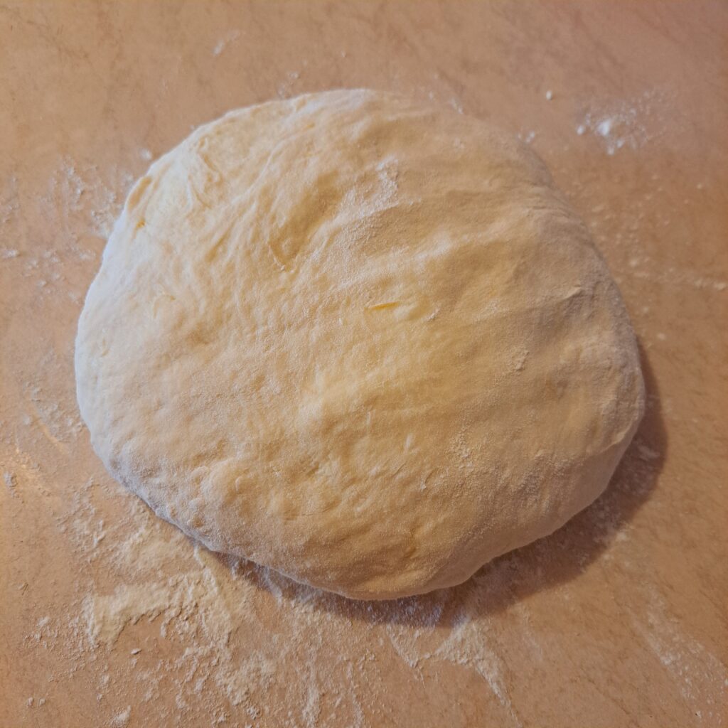 Smooth rested dough placed on a work surface, prepared for the first rolling step.